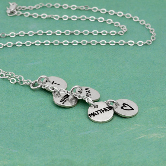 Side view of Custom Thai silver charm cascade mom necklace, personalized with 3 hand stamped kids names, on charm stamped with an initial, and one charm stamped with a heart, shown on green