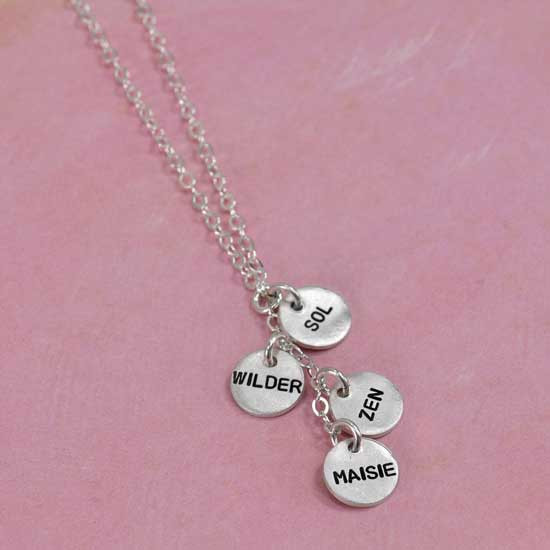 Custom Thai silver charm cascade necklace for mom, personalized with four hand stamped kids names, shown from the side on pink