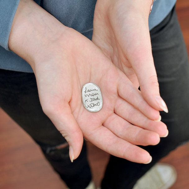 Handwritten note on fine pewter personalized oval pocket charm, shown in hands