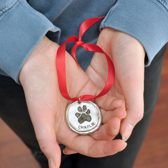 Custom fine pewter Christmas ornament, personalized with your dog or cat's pawprint, shown in model's hands