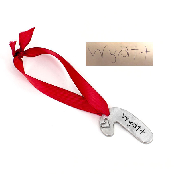Side view of custom fine pewter candy cane ornament, personalized with child's actual handwritten signature, hung on a red ribbon, and shown on white