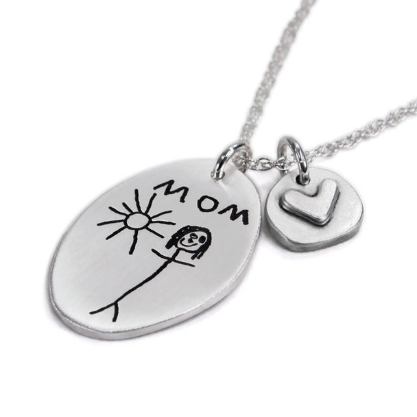 Side view of handmade sterling silver oval custom engraved with child's drawing of Mom and the sun. Paired with silver disc with silver raised heart, hung on a silver ball chain.