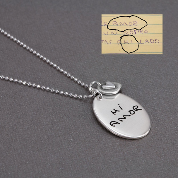 Side view of handmade sterling silver oval custom engraved with words taken from husband's handwritten note. Paired with silver disc with silver raised heart, hung on a silver ball chain
