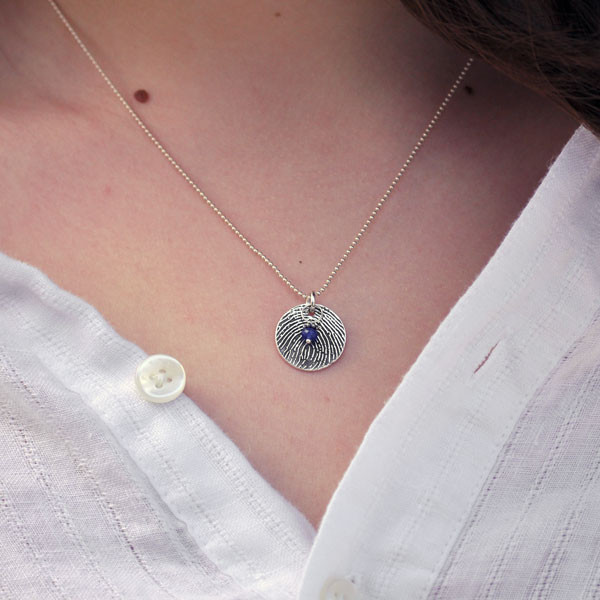 Close up of round sterling silver fingerprint necklace with birthstone on model