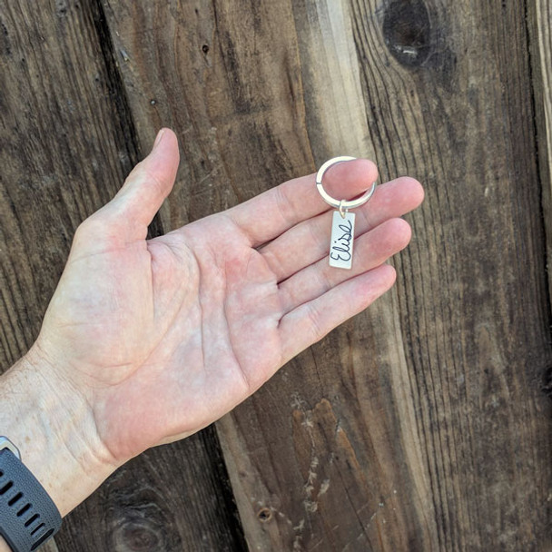 Silver handwriting key ring shown in a model's hand