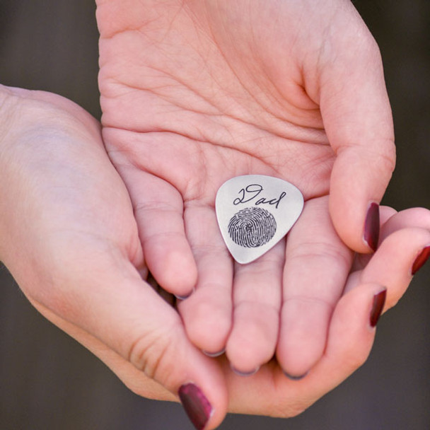 Custom memorial silver guitar pick, engraved with Dad's signature and fingerprint, held in model's hands