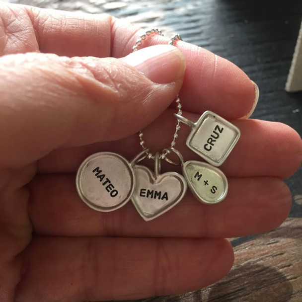 Sterling silver hand stamped raised edge charms on a mother's necklace, shown close up in hand