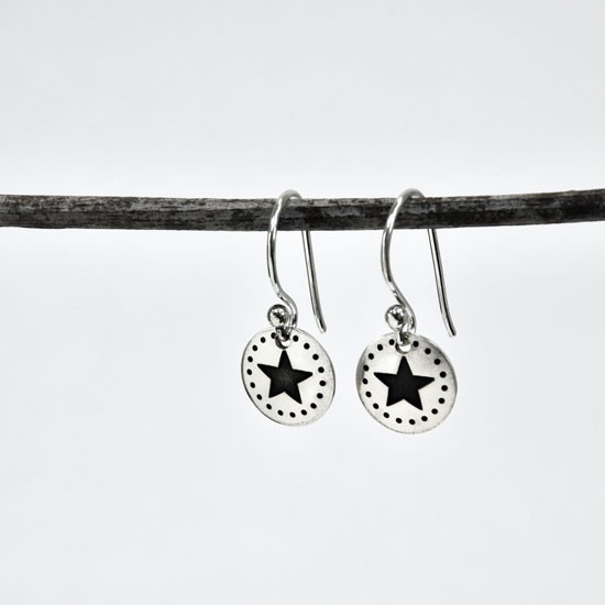 Handmade sterling silver star earrings with dotted border on sterling silver ear wires, shown shown hanging from a twig