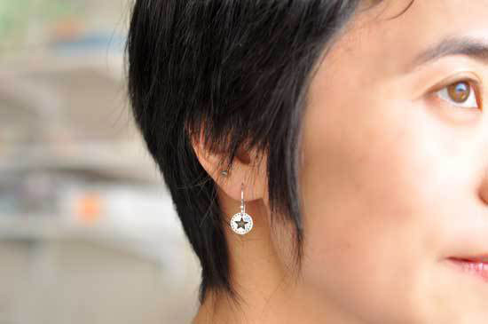 Handmade sterling silver star earrings with dotted border on sterling silver ear wires, shown on a model