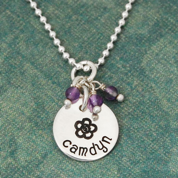 Custom sterling silver disc with stone cluster, personalized with hand stamped flower & child's name, shown on green