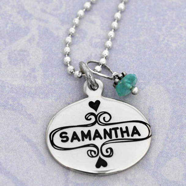 Close up view of silver Sweet Frame oval charm necklace personalized with daughter's name stamped in the middle, hung with blue apatite stone