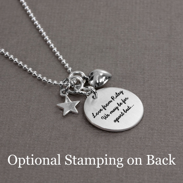 Side view of stamped Under the Same Moon Necklace, with silver charms on silver chain, personalized with stamped message on the back