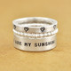 Silver custom wide band ring hand stamped with the words, "You are my sunshine", shown with other rings