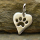 Silver heart charm with paw shape cut out of the middle, shown against a stone