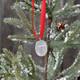 View hung on a tree of the front of custom handwriting memorial Cross Ornament, featuring a raised cross on a hand sculpted fine pewter oval, hung on a red ribbon