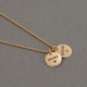 Hand stamped custom Gold Name Discs necklace personalized with kids names and symbols, shown close from the side on gray