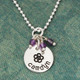 Custom sterling silver disc with stone cluster, personalized with hand stamped flower & child's name, shown on green