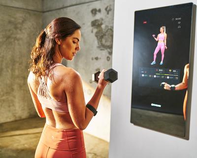 A woman is lifting a dumbbell in front of a mirror - image