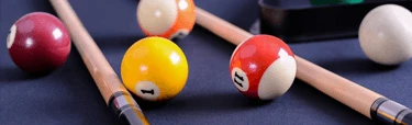 Billiard balls and Action pool cue sticks resting on a pool table, representing beginner-friendly action cues and pool sticks for players just learning the game