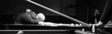 Black and white photo of a pool player lining up a shot at a billiard table, illustrating the technique and precision that comes from selecting the right action pool stick for your game