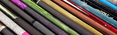 Close-up of colorful action cue sticks and pool cues from multiple brands fanned out, showcasing the variety of shaft designs, wraps, and finishes available from top billiards cue makers