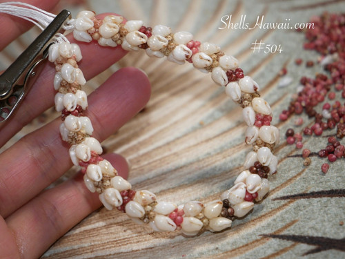 nibl_504
Close up Kipona style shell bracelet shown on hand before adding clasp, featuring genuine off white Momi shells with red, pink, brown, and black Kahelelani shell accents. Photo highlights the quality of the shells, detailed workmanship, and the balanced flow of shell colors and sizes throughout the bracelet.