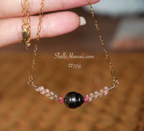 A delicate Hawaiian shell necklace hanging to showcase the dark silver-black Tahitian pearl and colorful hot pink, green, and Keʻokeʻo Kahelelani shells. A rare Hawaiian shell necklace that embodies coastal aesthetic jewelry.