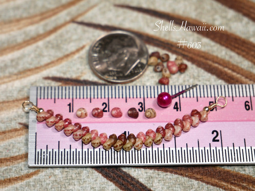 pd_603
Genuine Kahelelani shell necklace from Niʻihau shown beside a ruler and coin for size reference featuring Keʻokeʻo, pink flower, brown, and deep red burgundy shell colors in a refined curved design.