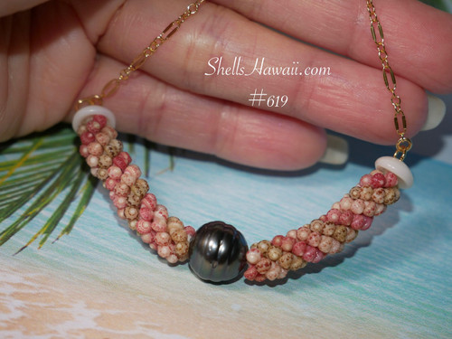 pd_619
Close-up full necklace view displayed across a hand showing the overall shape and curve of this handcrafted triple strand poepoe Kahelelani shell necklace with pink, green, and keʻokeʻo shells surrounding a baroque peacock Tahitian pearl centerpiece.