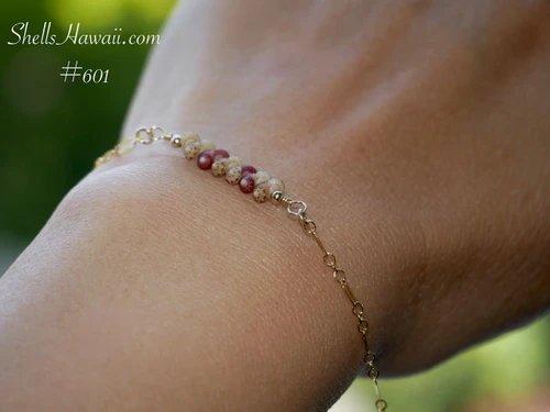 nibl_601
Close-up center view of the minimalist Kahelelani shell bracelet worn on wrist showcasing the delicate floating shell design with green Niʻihau shells and burgundy Kauaʻi shells connected by fine 14k gold filled chain.