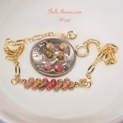 Authentic Niʻihau shell bracelet displayed beside a dime on a white dish showing the tiny scale and natural beauty of genuine Kahelelani shells in keʻokeʻo, ʻōmaʻomaʻo green, and pink flower tones accented with 14k gold filled chain. Delicate handcrafted Hawaiian shell jewelry with elegant minimalist island style.