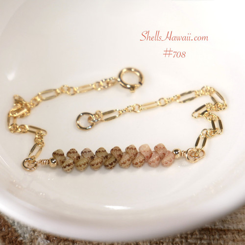 Authentic Niʻihau shell bracelet displayed on a white dish featuring genuine Kahelelani shells arranged in a soft ombré blend of ʻōmaʻomaʻo green and keʻokeʻo tones accented with delicate gold filled chain. Elegant handcrafted Hawaiian shell jewelry with refined minimalist coastal style.