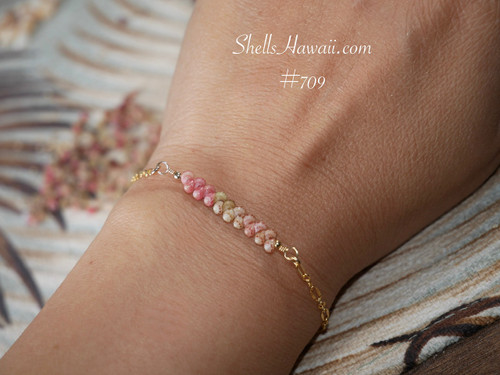 Pink ombré Kahelelani Hawaiian shell bracelet worn on wrist featuring genuine Niʻihau shells in soft ʻākala pua pink flower, ʻōmaʻomaʻo green, and keʻokeʻo tones. Elegant everyday Hawaiian jewelry with delicate coastal style and refined island inspired design.