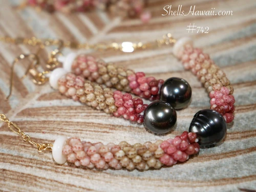 Handcrafted Triple Strand Poepoe Kahelelani shell necklace from Niʻihau held against a natural green background, showing colorful size 11 shells and a medium-dark baroque Tahitian pearl