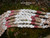 Close-up of triple-strand long Niʻihau shell lei in traditional Kipona style featuring white Keʻokeʻo Momi shells poked in coconut style to resemble the male coconut flower and tied in Pikake technique along with beautiful two-strand Poepoe sections created with pink flower, ʻŌmaʻomaʻo green, and red burgundy Kahelelani shells.