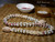 Full layout of Kipona style Niʻihau shell lei arranged on woven mat, featuring white Momi shells and Kahelelani shells in pink, burgundy, and green tones, finished with off-white granulated cowrie shell clasp, showing balanced design, natural texture, and handcrafted Hawaiian shell jewelry ニイハウシェル ネックレス
