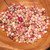 Close-up of genuine mixed color Kahelelani shells from Niʻihau displayed inside a wooden bowl with a regular head pin for size reference. Tiny Hawaiian shells in pink, burgundy, white, brown, and spotted tones with natural luster, perfect for Heliconia, Poepoe, Kipona, minimalist earrings, pendants, and traditional Niʻihau shell jewelry making.