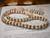 Full lei view laid in soft curve showing four-strand Kipona design, natural mix of white and lightly striped Momi shells from Niʻihau with warm chocolate Kahelelani shells from Kauaʻi, elegant handmade Hawaiian shell necklace set $1450