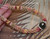 Close up Niʻihau shell lei in Double-Double Kipona style held in hand, featuring Kahelelani Poepoe center in pink, yellow, brown, and soft cream tones with Tahitian pearl focal, detailed colorful tiny Niʻihau shells and fine handcrafted Hawaiian shell jewelry