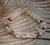 Handmade Niʻihau shell bracelet kipona style with light tone momi shells and mixed kahelelani shells red burgundy pink flower green colors full view #395
