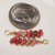 Tiny Niihau Kahelelani shell earrings shown next to a dime for size comparison, featuring red, burgundy, pink, green soft pink size 10 shells in a 3/4 inch drop design.