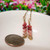 Tiny Kahelelani Niihau shell earrings shown next to a U.S. dime for size comparison, featuring green, burgundy and pink tone shells in a 3/4 inch minimalist drop design.