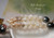 Close up Hawaiian shell lei showing transition between Momi shells in off white (Keʻokeʻo), yellow (Lenalena), and brown spotted (Onikiniki) tones with pink Kahelelani shell accents and dark peacock Tahitian pearl, highlighting smooth luster, clean drilling, and precise Kipona tying technique