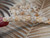 Close up of Momi shells held between fingers during the creation process, showing the quality of the shells, natural luster, and fine workmanship of this traditional Crown Flower style Niʻihau shell bracelet design.