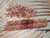 A professional, full-length photograph of the 3-inch Hawaiian Poepoe-style shell earrings, as seen in image 3643.7.jpeg. The two earrings are meticulously crafted from small, high-grade Kahelelani shells collected on Kauaʻi, showing a distinct ombre color gradation. The pattern shifts from soft yellow and natural brown to pink and a central rich burgundy. The intricate texture and 14k gold-filled ear wires are clearly displayed against a simple, textured surface.