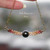 Close-up of an artisan shell jewelry piece hanging, highlighting the natural luster of the dark silver-black Tahitian pearl and the colorful texture of the Kahelelani shells. A perfect example of modern coastal jewelry.