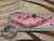 Genuine Kahelelani shell necklace from Niʻihau shown beside a ruler and coin for size reference featuring Keʻokeʻo, pink flower, green, and deep red burgundy shell colors in a delicate curved floating design.