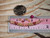 Genuine Kahelelani shell necklace from Niʻihau shown beside a ruler and coin for size reference featuring Keʻokeʻo, soft pink, green, and deep red burgundy shell colors in a refined floating design.
