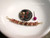 Handcrafted curved floating shell necklace from Hawaiʻi displayed beside a coin for size reference featuring Keʻokeʻo, Niʻihau green, and Kauaʻi burgundy Kahelelani shells.