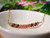 pd_612
Close-up view of the minimalist curved floating shell necklace displayed in a white ceramic dish showcasing the overall pendant design, flowing ombré color pattern, and delicate handcrafted arrangement of genuine Kahelelani shells from Niʻihau in green, burgundy, and pink tones.